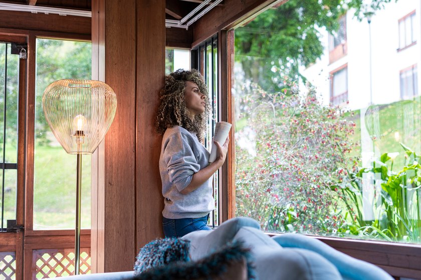 Frau steht am Fenster und tankt Licht