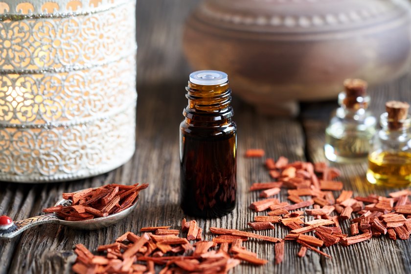 A dropper bottle of aromatherapy essential oil with red sandalwood chips and an aroma lamp in the background A dropper bottle of aromatherapy essential oil with red sandalwood chips and an aroma lamp in the background